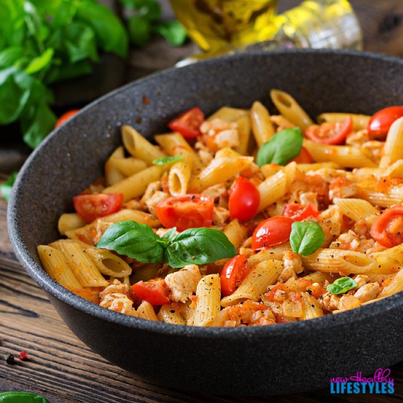 Penne pasta with chicken and tomatoes in a pan on a wooden table.