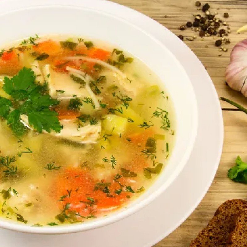 A bowl of chicken soup with vegetables and bread.